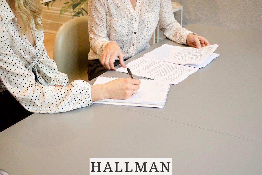 woman signing on white printer paper beside woman about to touch the documents